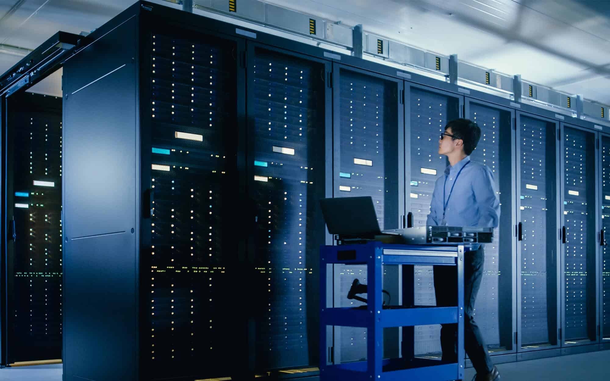 Side view of a man standing in a server room with a computer cart